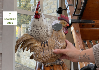 Una mano con braccialetto e tatuaggio botanico tocca un galletto decorativo accanto a una gallina.